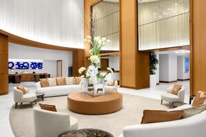 Eine großzügige Lobby mit einer zentralen Sitzecke, einem Empfangsbereich und einem großen Fenster.