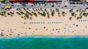 An aerial view of a beach with rows of umbrellas and beach chairs, palm trees, and a road with cars. - Conrad Fort Lauderdale Beach (Fort Lauderdale)