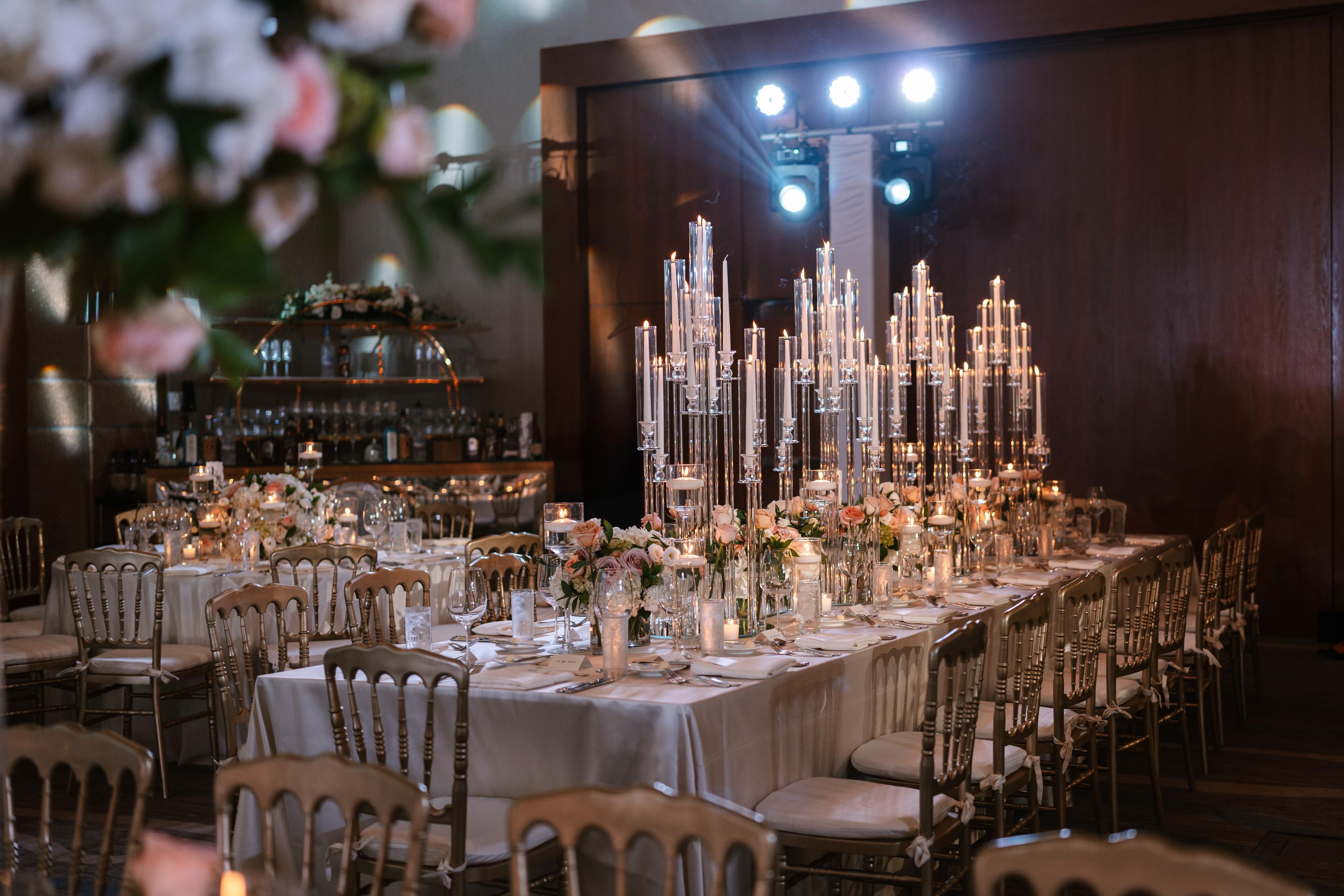 Une salle à manger élégante, avec de longues tables, des bougies et des compositions florales.