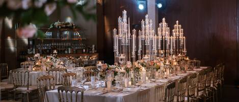 Une salle à manger élégante, avec de longues tables, des bougies et des compositions florales.