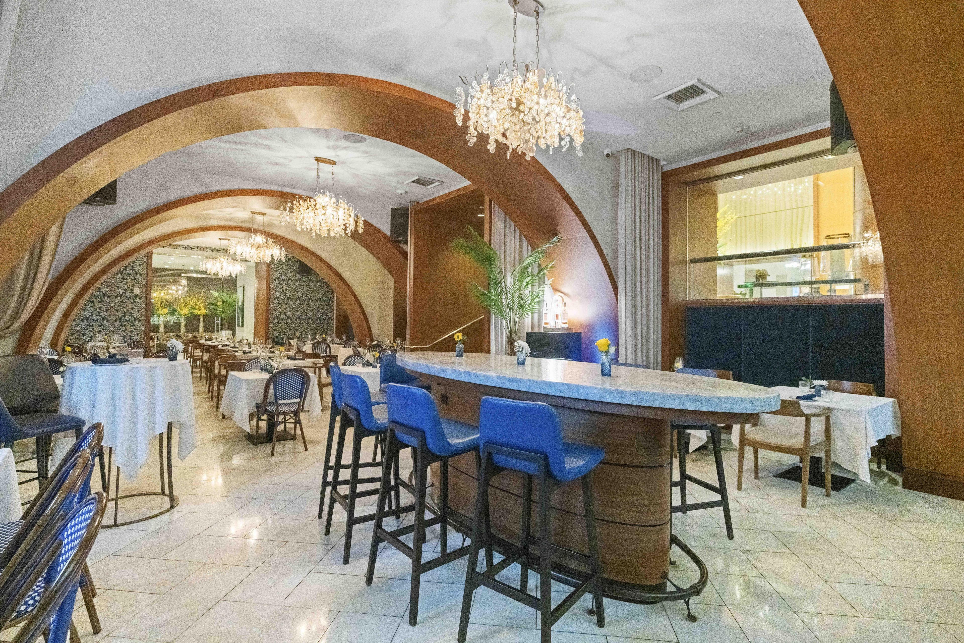 Ein Restaurant mit Barbereich, ausgestattet mit blauen Barhocker, einer Marmorplatte und einer Kristallleuchter.