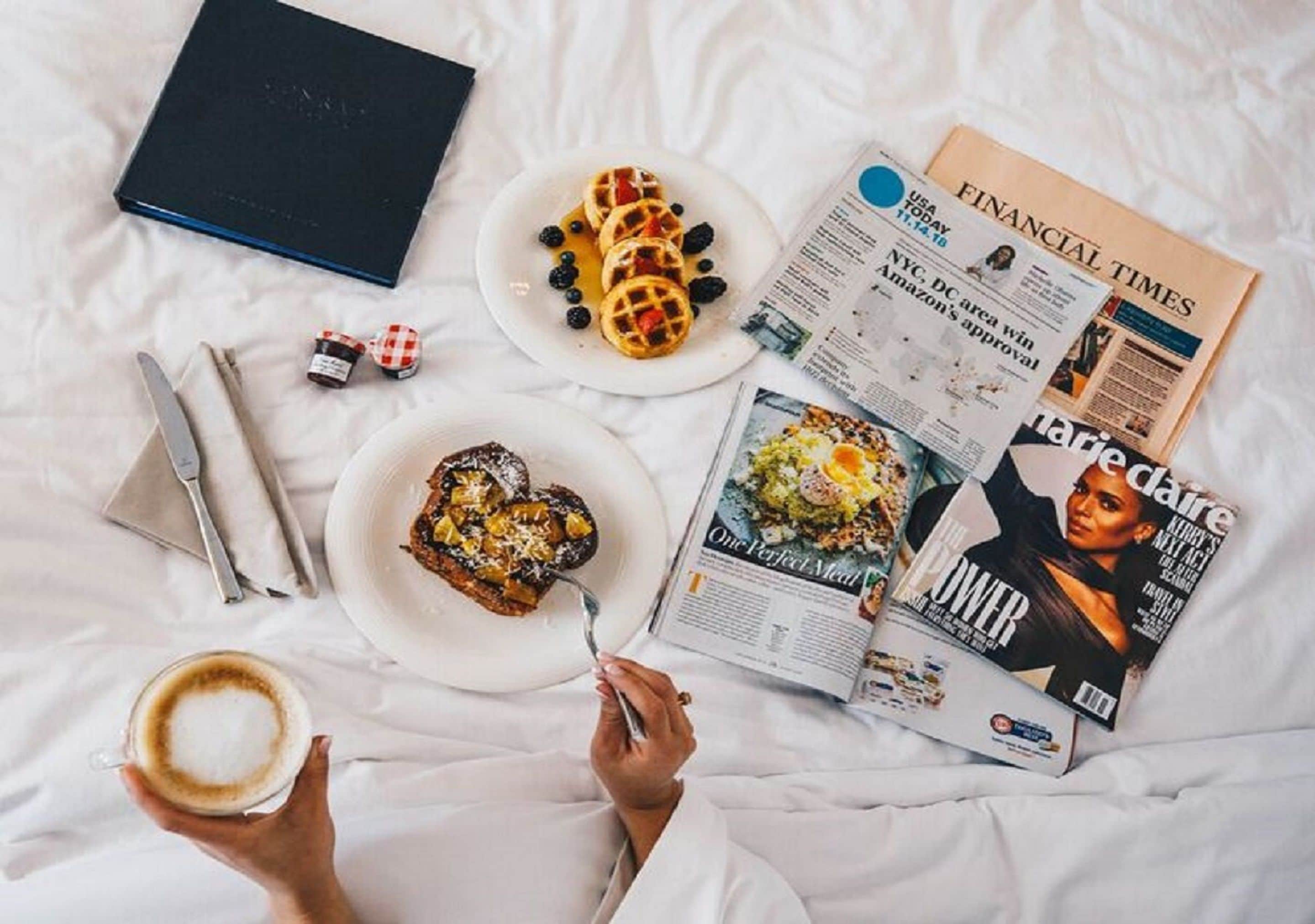 Una cama, un libro, un plato de gofres, un plato de pimientos rellenos, una revista, una taza de café y un par de gafas.