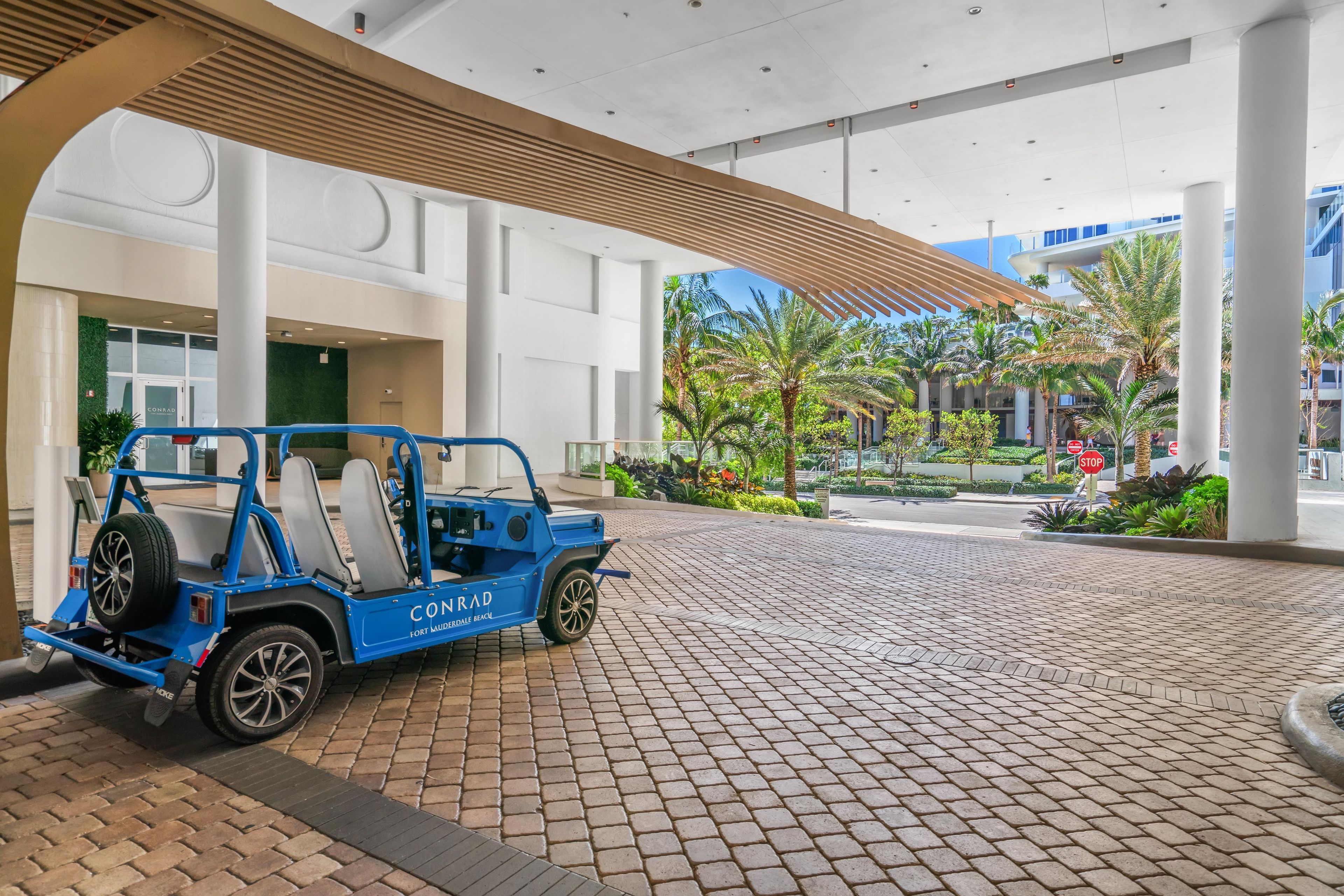 A blue golf cart parked in a paved area with a modern building in the background.