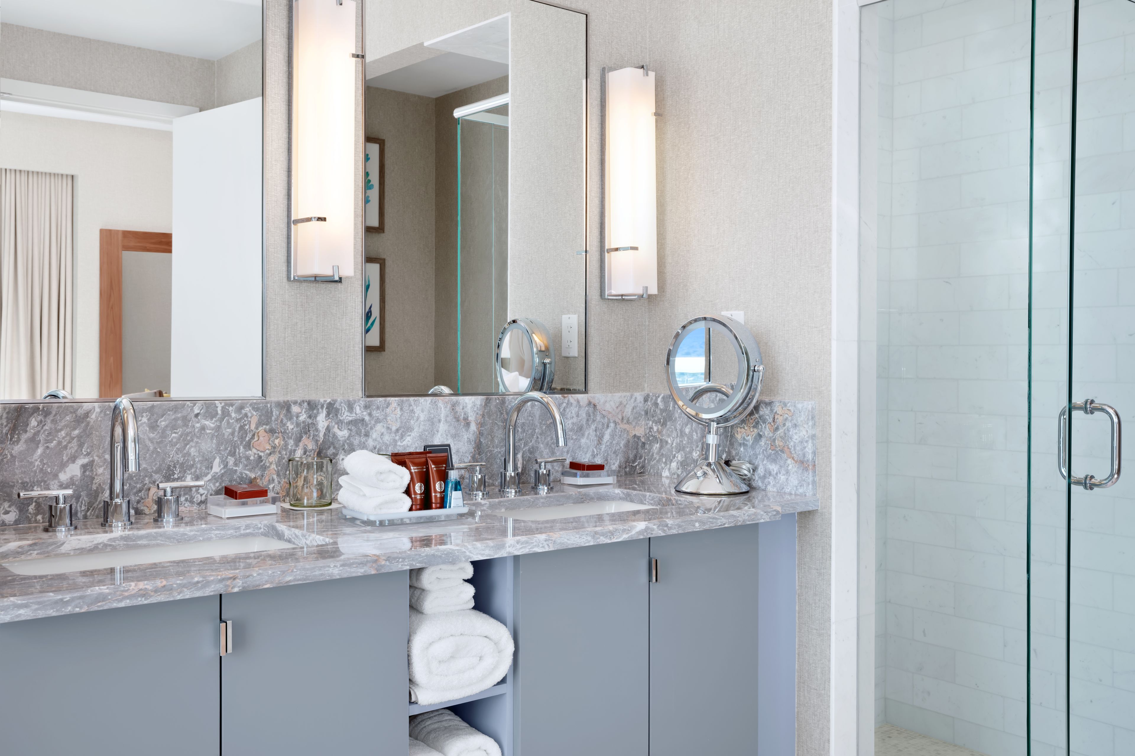 A modern bathroom with a marble countertop, a large mirror, a glass shower enclosure, and neatly folded towels.