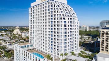 Un hotel moderno de gran altura con una fachada curva distintiva, varios balcones y una zona de piscina en la azotea.