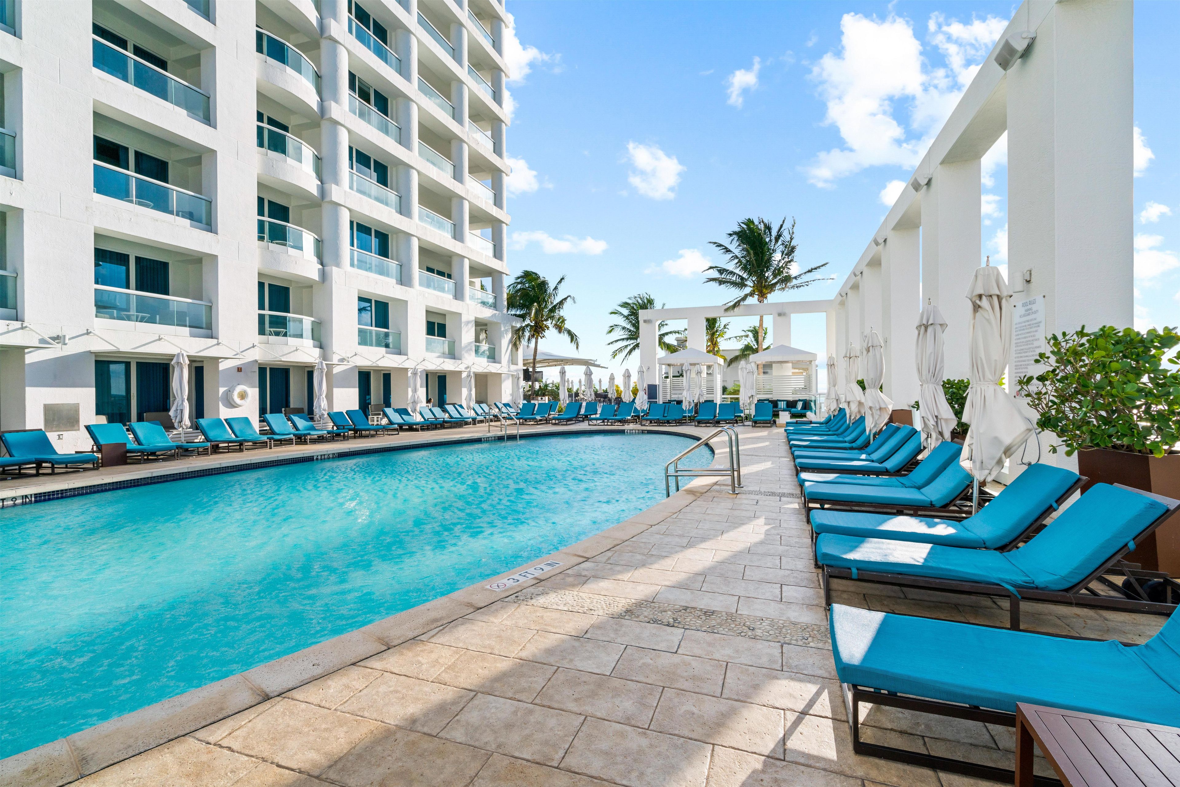 Un espace piscine avec des chaises longues et un bâtiment doté de nombreux balcons.