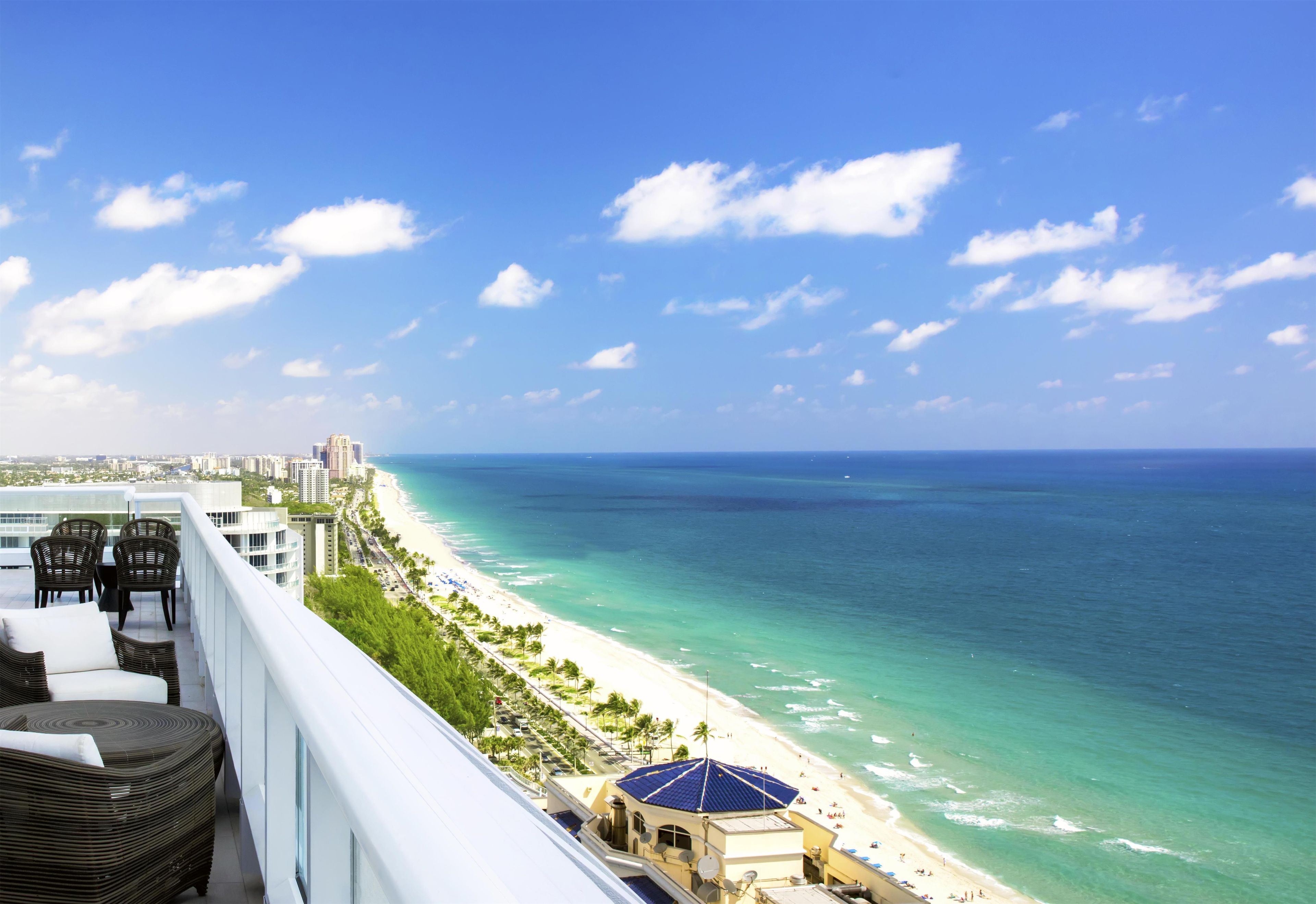 A high-rise hotel with a balcony overlooking a beach and ocean.