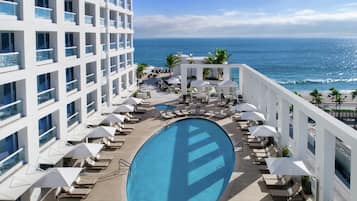 A rooftop pool with lounge chairs and umbrellas, overlooking a beach and ocean.