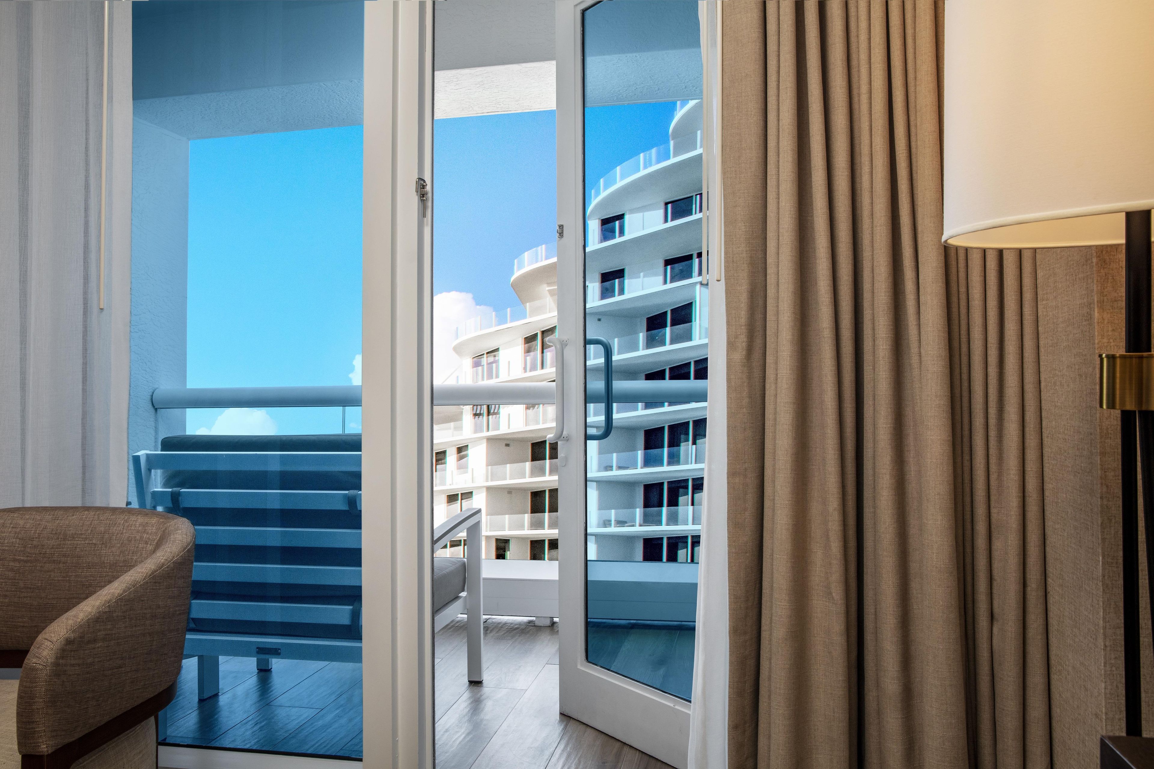 A hotel room with a balcony, a chair, and a view of a building with multiple balconies.