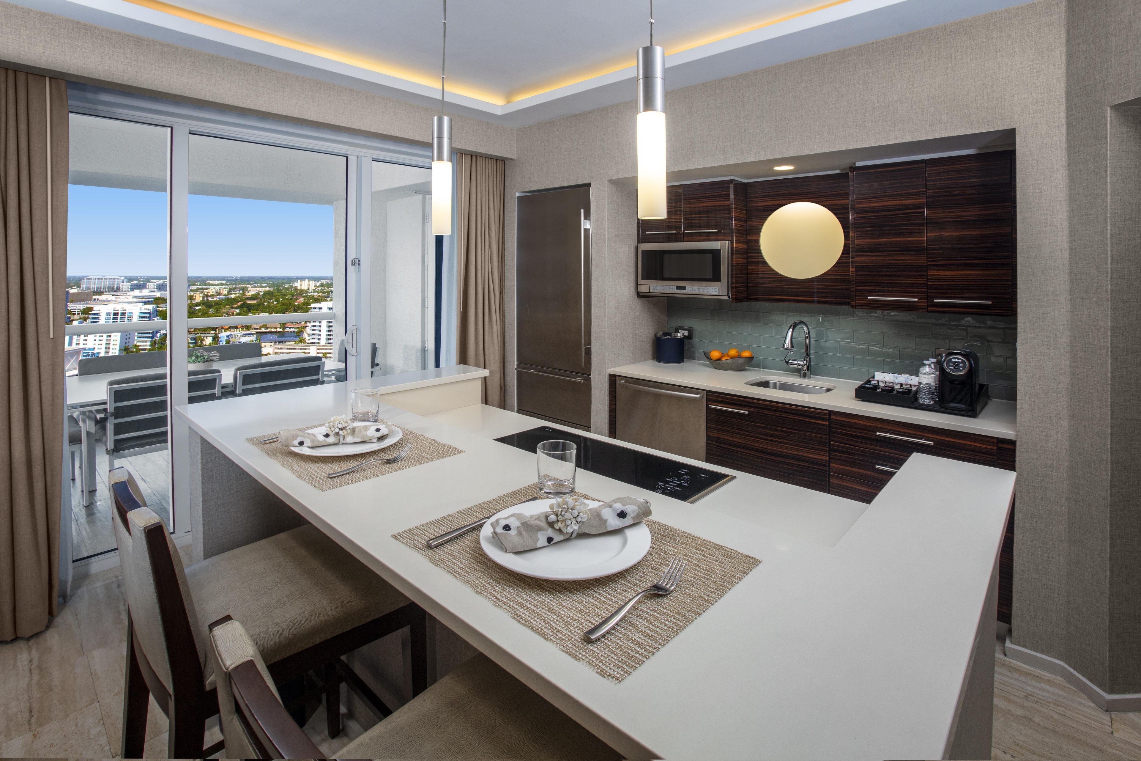 A modern kitchen with a central island, a dining area with a view, and a large window.