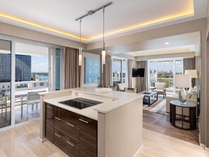 A modern hotel room with a large window, a flat-screen TV, a dining area, and a kitchen with a built-in stove. - Conrad Fort Lauderdale Beach (Fort Lauderdale)
