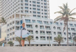 A person holding a surfboard in front of a modern building with circular windows and palm trees. - Conrad Fort Lauderdale Beach (Fort Lauderdale)