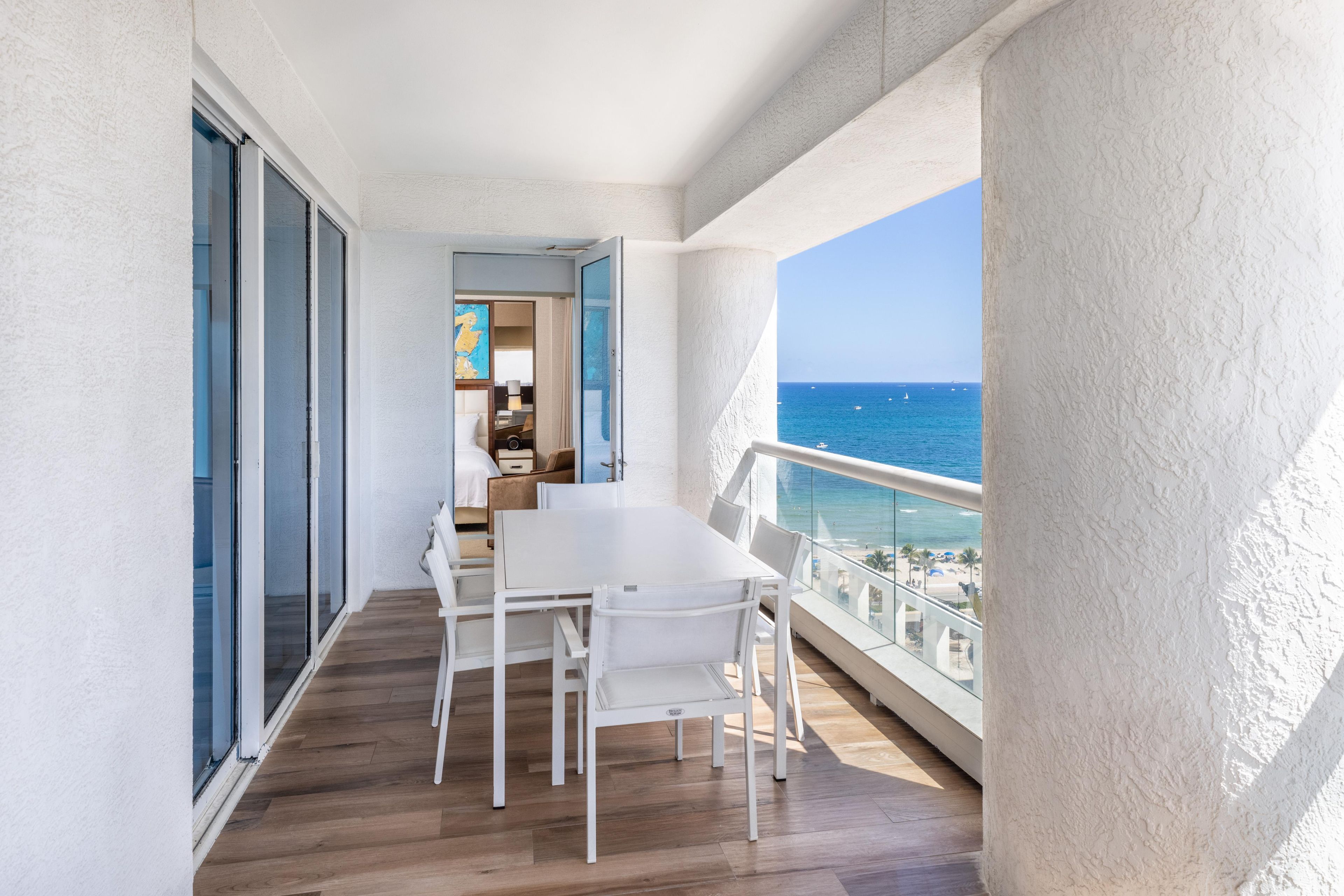 Un balcon avec une table et des chaises pour prendre les repas, une vue sur la mer et un aperçu de l’intérieur.