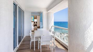Un balcon avec une table et des chaises pour prendre les repas, une vue sur la mer et un aperçu de l’intérieur.