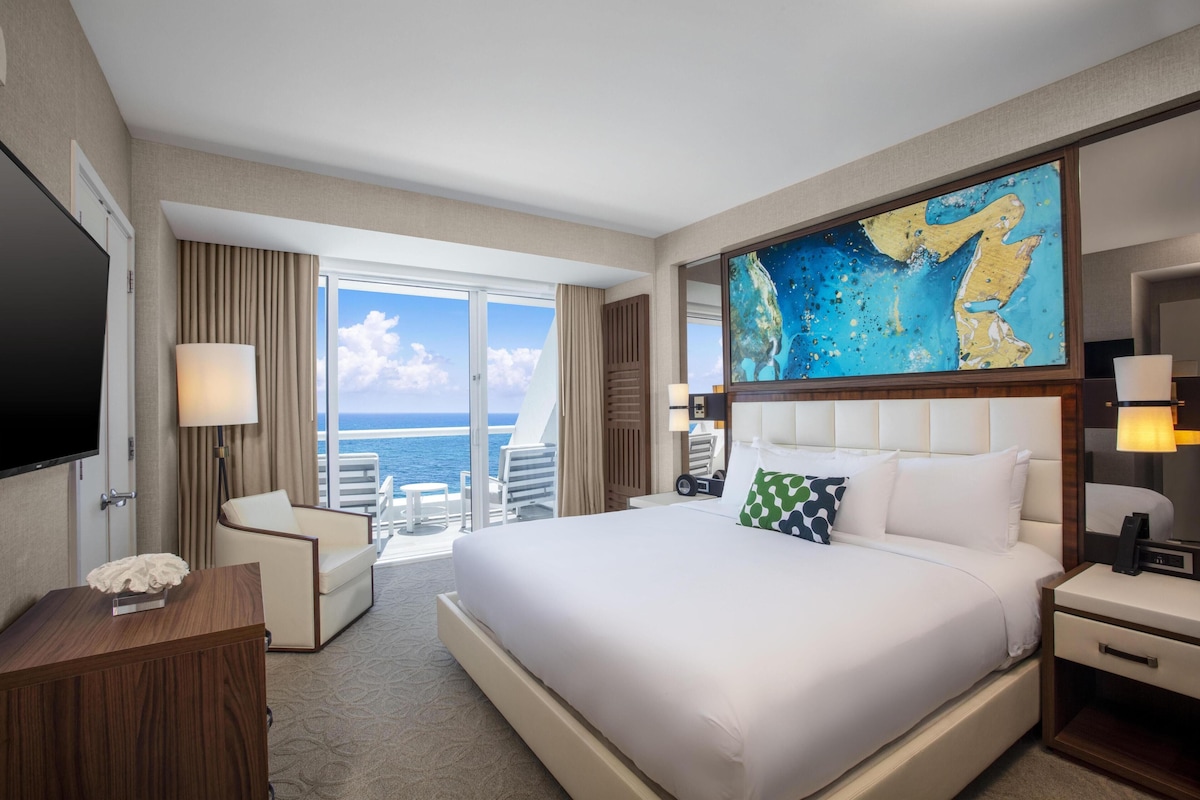 A hotel room with a large bed, a desk, a chair, a TV, and a painting.