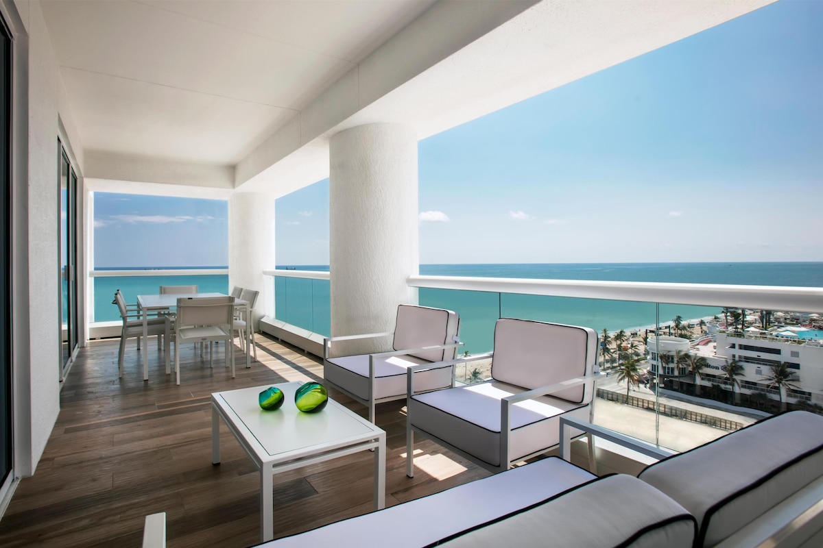 A balcony with a view of the ocean, furnished with a table, chairs, and a sofa.