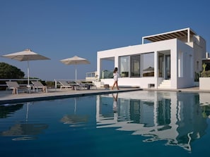 A modern poolside area with lounge chairs and umbrellas, a clear pool, and a contemporary building with large windows.