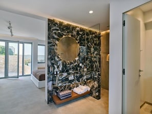 A modern bathroom with a stone wall, a round mirror, and a shelf with towels.