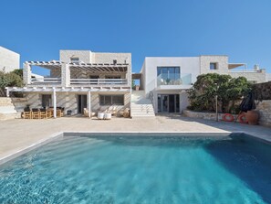 Una villa moderna con piscina, mobiliario exterior y fachada de piedra.