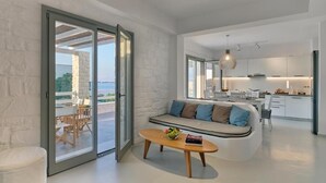 A modern living room with a sofa, a coffee table, and a dining area with chairs. - Empire Luxury Villas (Paros)