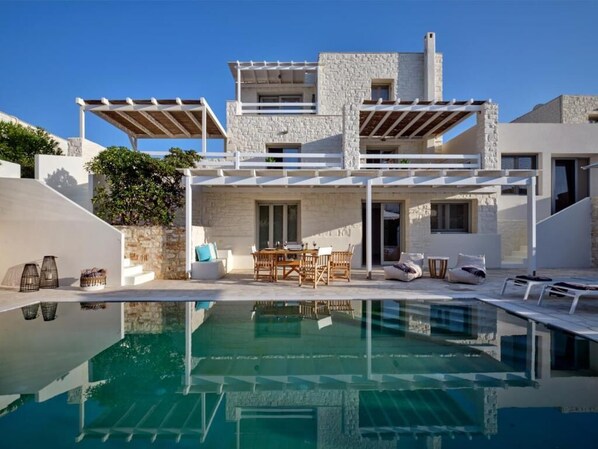 Una villa moderna con piscina, fachada de piedra y zona de estar exterior.