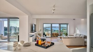 A modern kitchen with a breakfast setup, a dining area with a view, and a living room with a sofa and a TV. - Empire Luxury Villas (Paros)