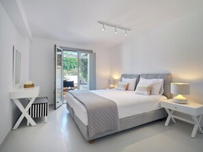 Un dormitorio moderno con una cama grande, mesitas de noche, un taburete pequeño y una puerta corrediza de vidrio que da a un espacio al aire libre.