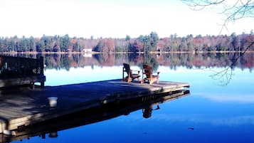 A wooden dock extending into a calm lake with a clear reflection of the surrounding trees.