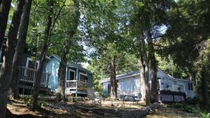 A cabin with a deck, surrounded by trees and a stone wall. - Black Lake Cabins (Muskoka Lakes)