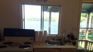 A kitchen with a stove, sink, and window overlooking a body of water. - Black Lake Cabins (Muskoka Lakes)