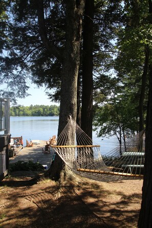 A hammock tied between two trees, a wooden dock, and a lake view.