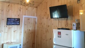 A wooden-paneled room with a white refrigerator, a microwave, a flat-screen TV mounted above the refrigerator, and a hanging light fixture. - Black Lake Cabins (Muskoka Lakes)