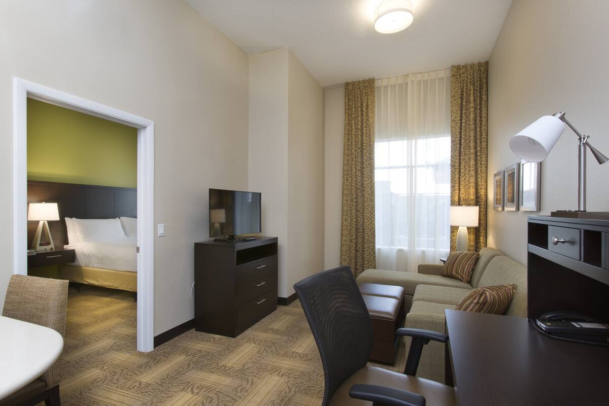 A hotel room with a bed, a desk, a chair, a television, and a lamp.