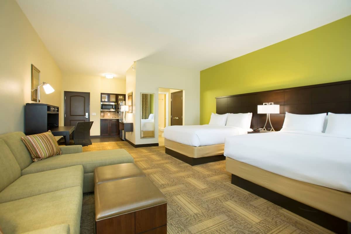 A hotel room with a large bed, a sofa, a small desk, and a kitchenette.