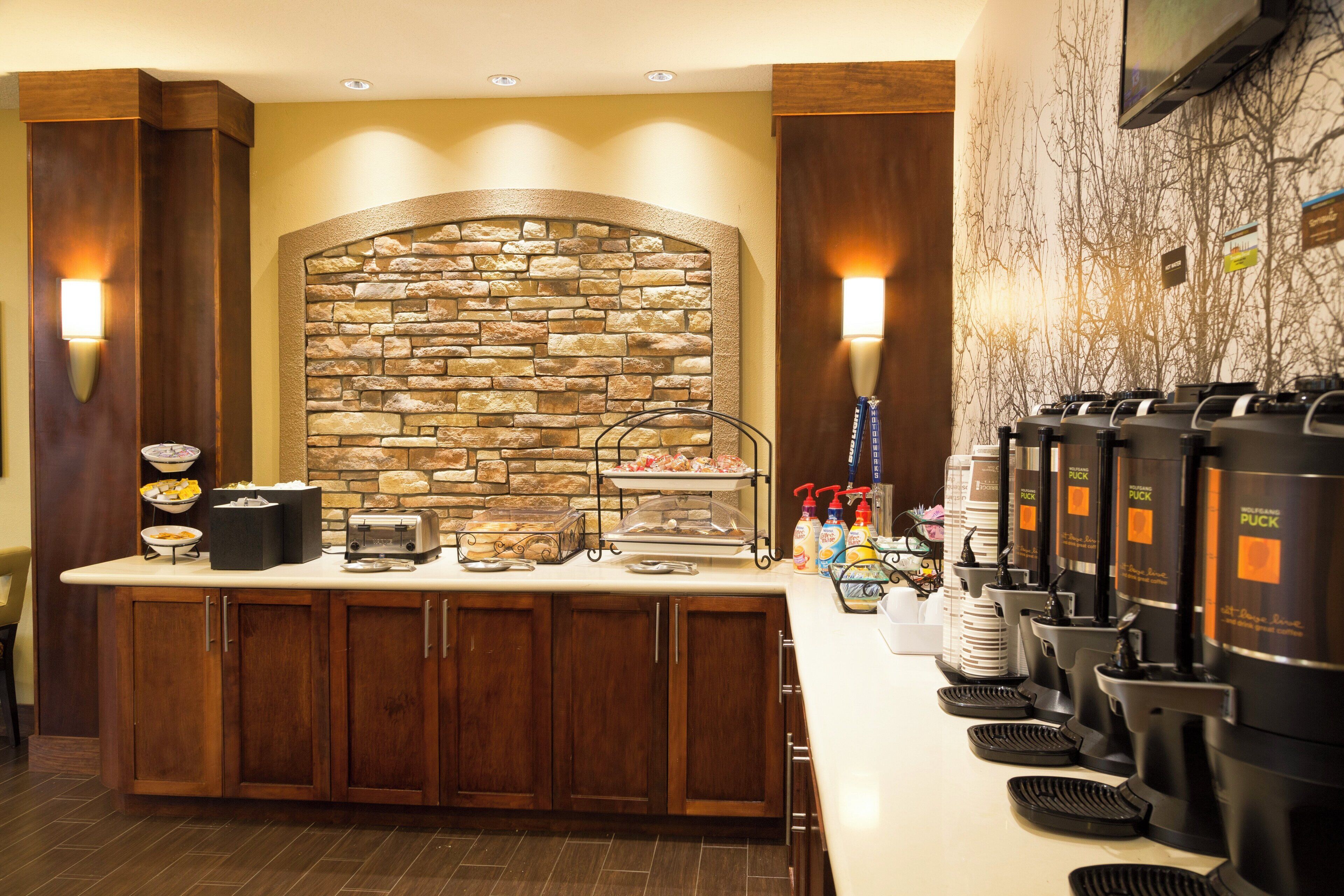 A breakfast bar with a stone wall backdrop, a coffee station, and a buffet area with trays.