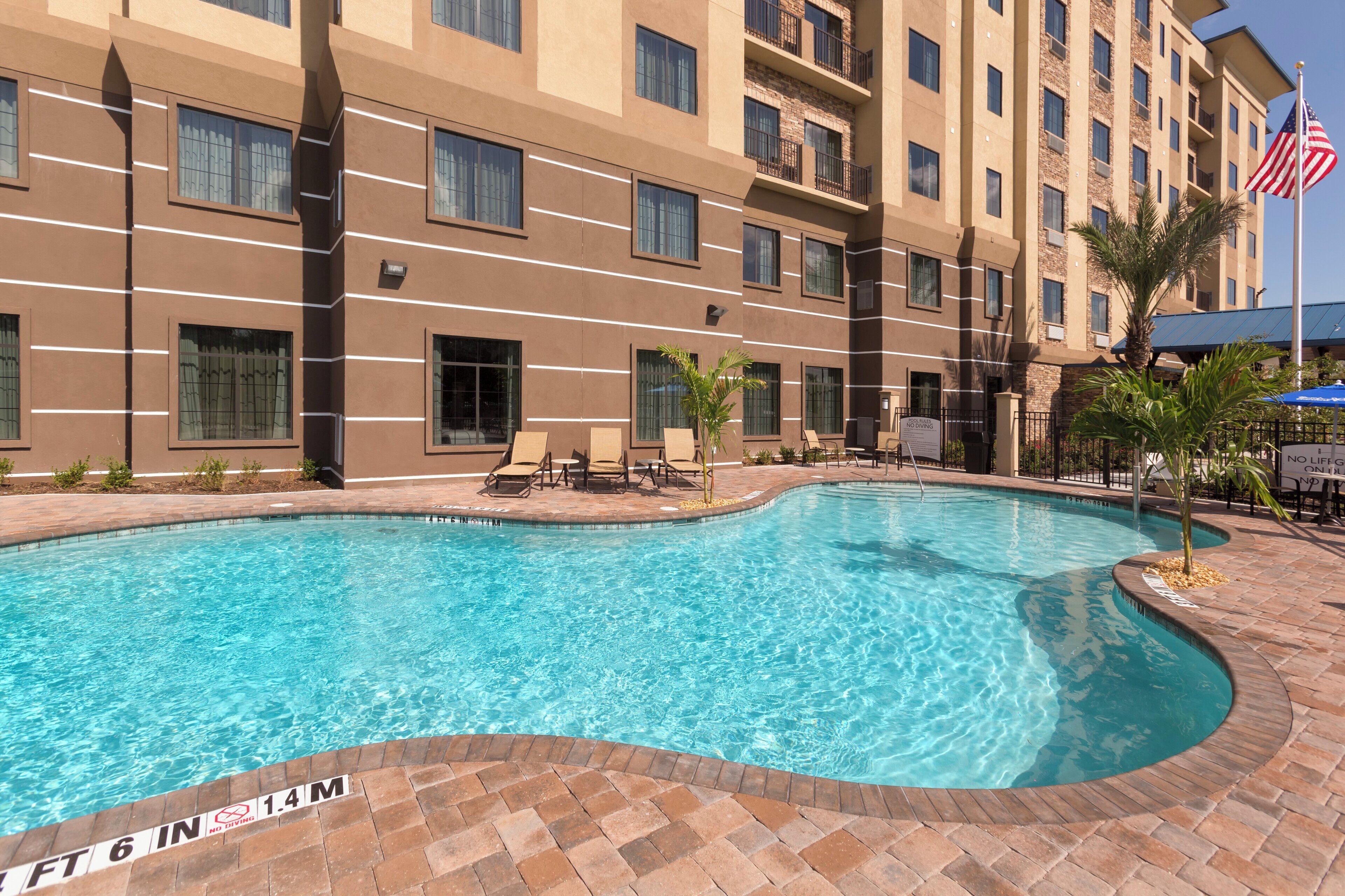 A hotel with a swimming pool, lounge chairs, and a flag.