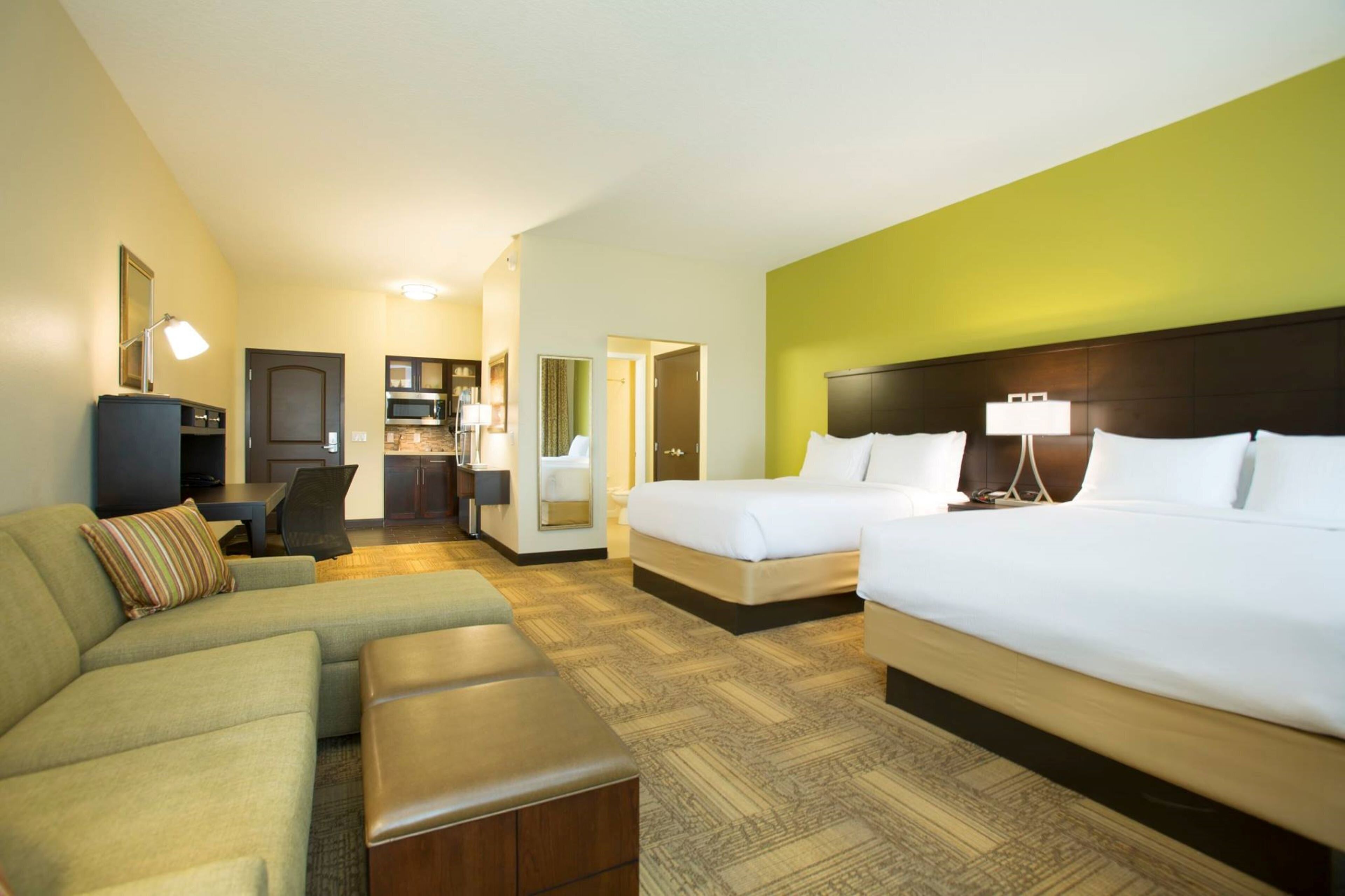 A hotel room with a large bed, a sofa, a small desk, and a kitchenette.