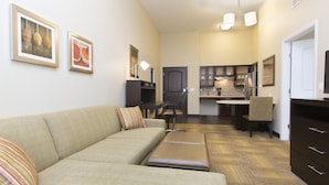 A living room with a sofa, ottoman, and a dining area with a table and chairs. There is a kitchen in the background with cabinets and a refrigerator. - Staybridge Suites Orlando at SeaWorld by IHG (Orlando)