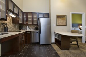 A modern kitchen with dark wooden cabinets, a stainless steel refrigerator, and a small island with a microwave.