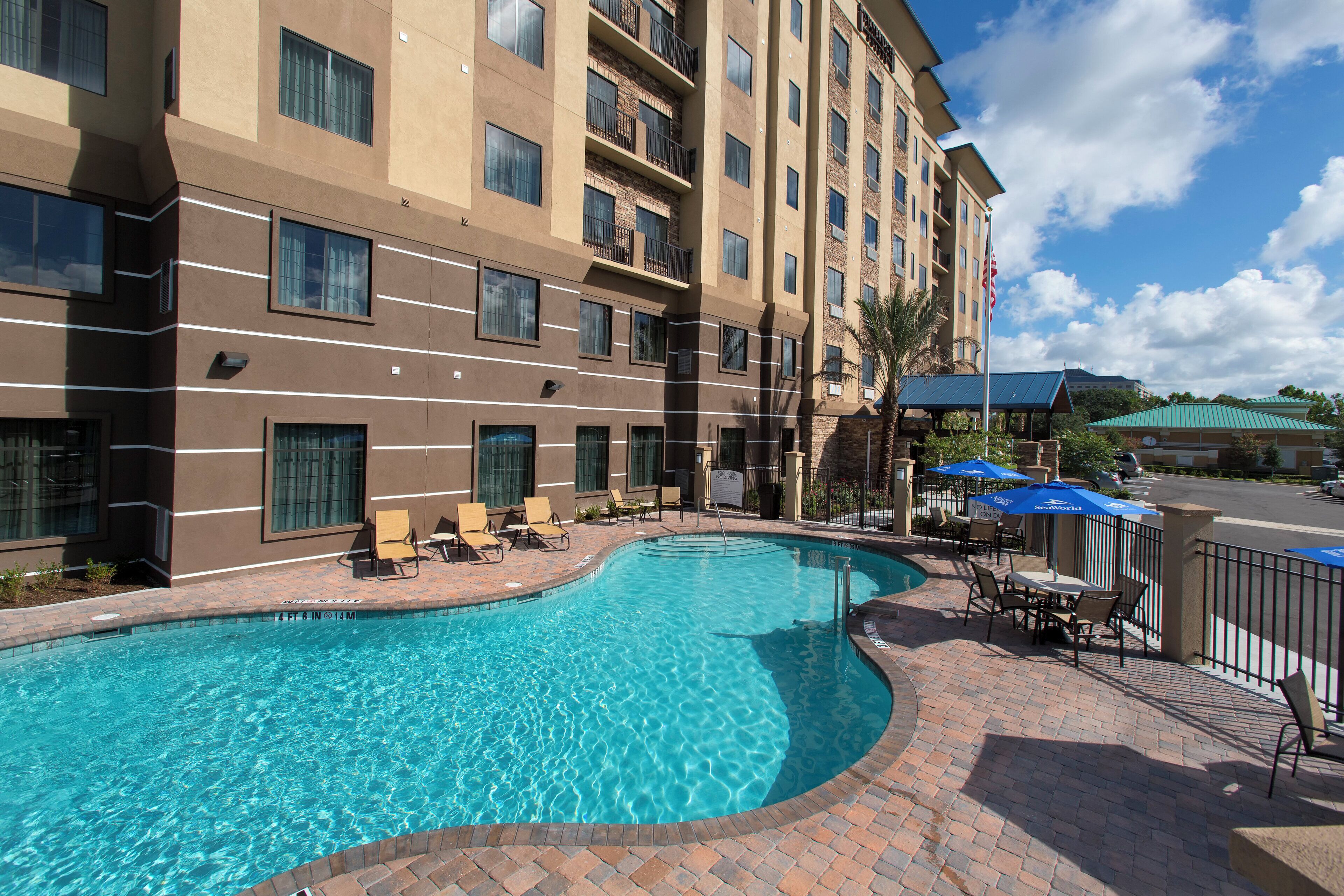 A hotel with a swimming pool, outdoor seating, and a clear sky.
