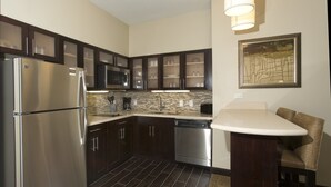 A modern kitchen with dark wood cabinets, stainless steel appliances, a tiled backsplash, and a dining area with a bar stool.