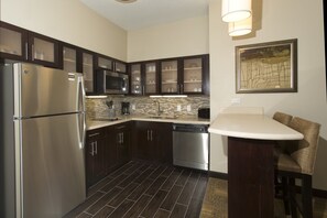 A modern kitchen with dark wood cabinets, stainless steel appliances, a tiled backsplash, and a dining area with a bar stool.