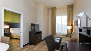 A hotel room with a bed, a desk, a chair, a television, and a desk lamp.