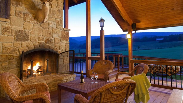 A stone fireplace with a log fire, wicker furniture, and a view of the landscape.