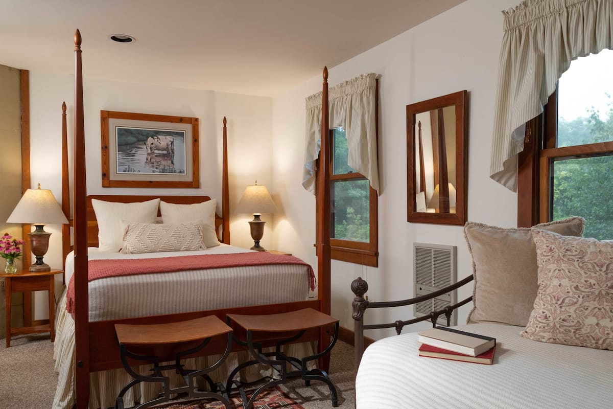 A four-poster bed with a headboard, two bedside tables with lamps, a small table, and a chair.