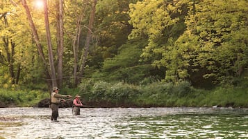 A river with two people fishing, surrounded by dense greenery and trees.