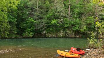 Un kayak naranja de un kayakista sobre la orilla rocosa de un río, rodeado de un bosque verde y frondoso.