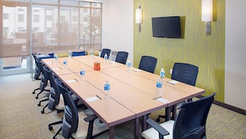 Un salón de conferencias con una larga mesa, sillas, botellas de agua y un televisor en la pared.