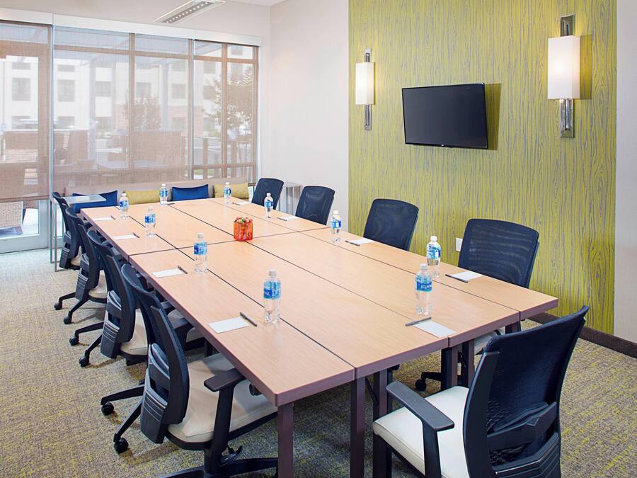 A conference room with a long table, chairs, water bottles, and a TV on the wall.