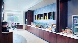 A modern hotel kitchen with a long counter, various food items, and a refrigerator. - Springhill Suites by Marriott Carle Place Garden City (Carle Place)